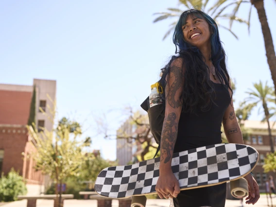 person holding a skateboard with brick buildings and palm trees visible in the background