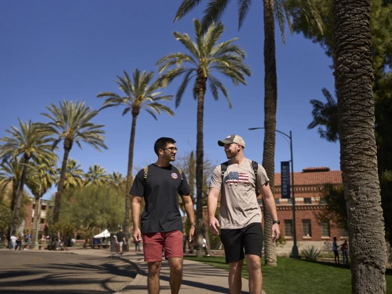 two people wearing backpacks walking on a sidewalk with palm trees visible in the background